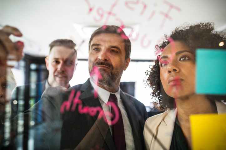 two men and one woman in front of a board